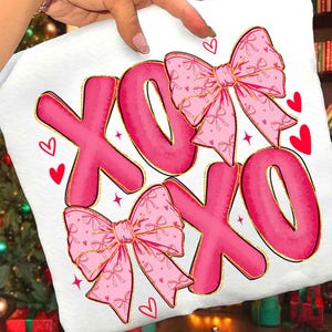 May include: White fabric with a pink "XOXO" design. The letters are outlined in gold and feature pink bows with gold trim. Red hearts and stars are scattered around the letters, creating a romantic theme.