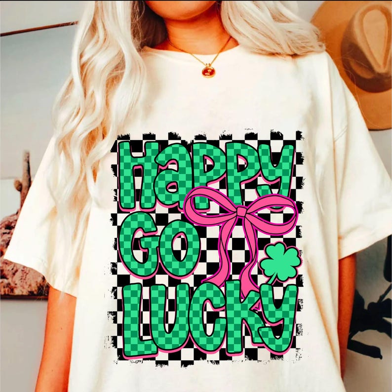 May include: White t-shirt with a green and black checkered design featuring the text "Happy Go Lucky" with a pink bow and a green shamrock.