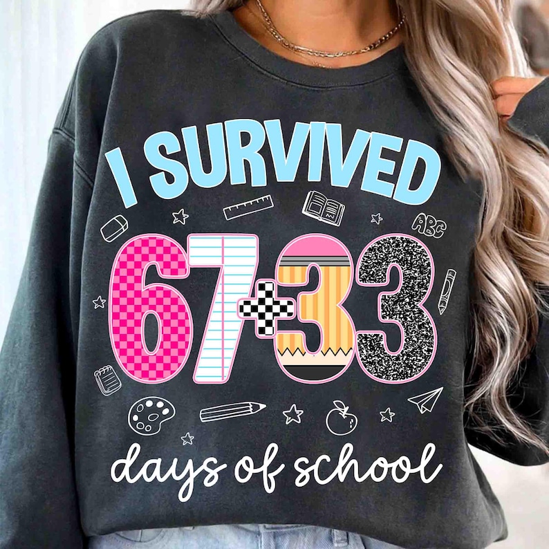 May include: Dark gray sweatshirt with the text "I SURVIVED 67+33 days of school" in light blue and white. The numbers are decorated with pink, black, and yellow patterns, and school-themed graphics.