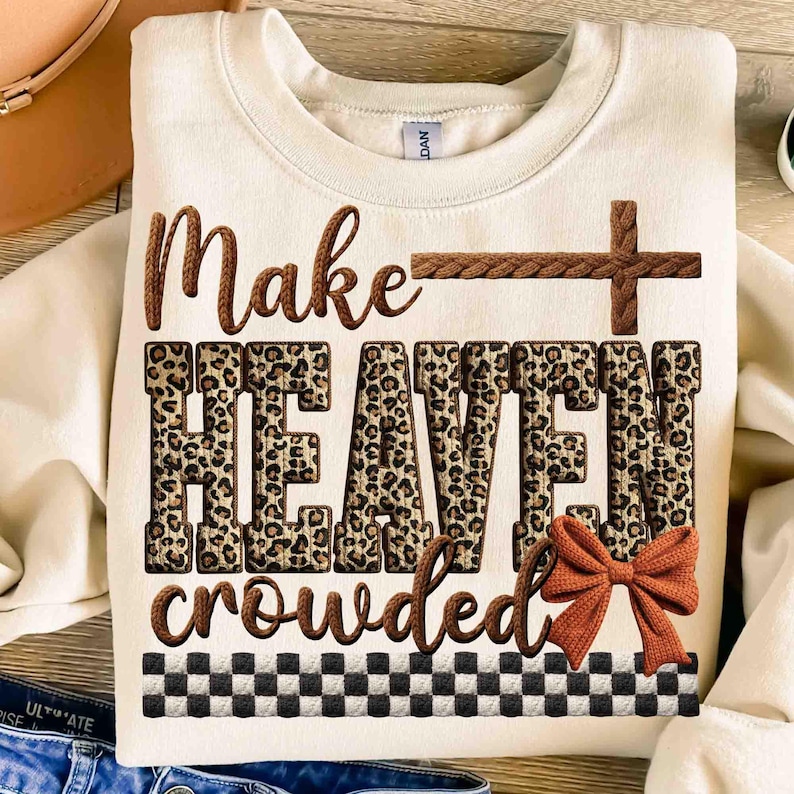 May include: Cream-colored sweatshirt with the phrase "Make HEAVEN crowded" in brown and leopard print. A brown cross and bow accent the design. A black and white checkered pattern is at the bottom.