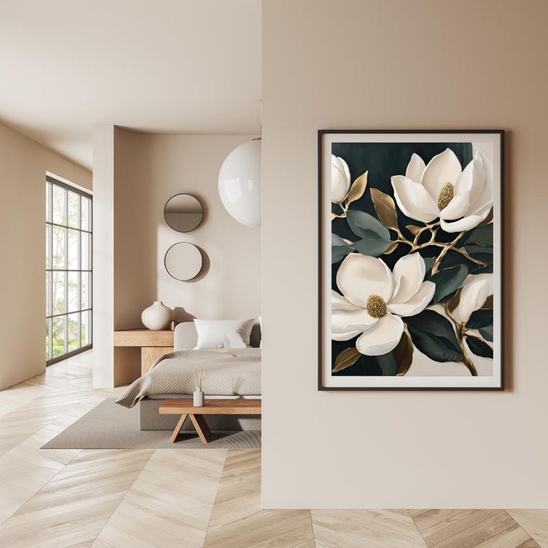 K&ouml;nnte beinhalten: Gerahmter Kunstdruck mit einer botanischen Illustration wei&szlig;er Magnolienbl&uuml;ten mit dunkelgr&uuml;nen Bl&auml;ttern und goldenen Akzenten. Das Kunstwerk ist vor einem dunklen Hintergrund und in einem schwarzen Rahmen gesetzt. Der Druck wird an einer beigen Wand gezeigt.