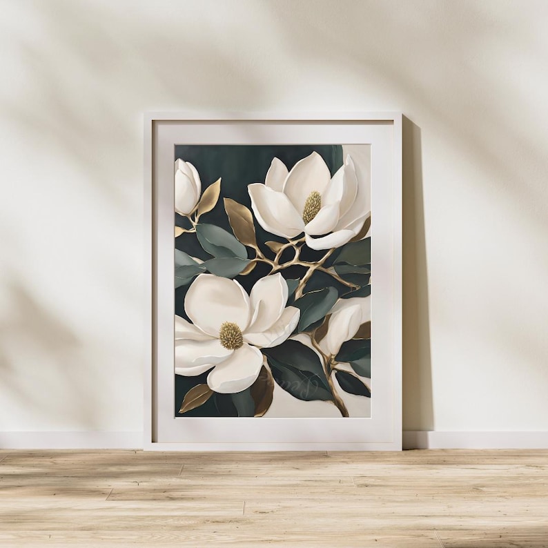 K&ouml;nnte beinhalten: Gerahmter Kunstdruck mit wei&szlig;en Magnolienbl&uuml;ten mit goldenen Akzenten und dunkelgr&uuml;nen Bl&auml;ttern. Das Kunstwerk ist vor einem dunklen Hintergrund platziert und mit einem wei&szlig;en Rahmen versehen, was einen auff&auml;lligen Kontrast erzeugt. Der Druck wird auf einem Holzboden pr&auml;sentiert.