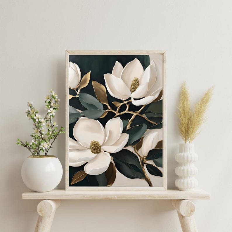 K&ouml;nnte beinhalten: Ein gerahmter Kunstdruck mit gro&szlig;en wei&szlig;en Magnolienbl&uuml;ten mit goldenen Zentren und Akzenten. Das Kunstwerk hat dunkelgr&uuml;ne und goldene Bl&auml;tter vor einem dunklen Hintergrund. Der Druck wird auf einem hellen Holzregal mit dekorativen Vasen ausgestellt.