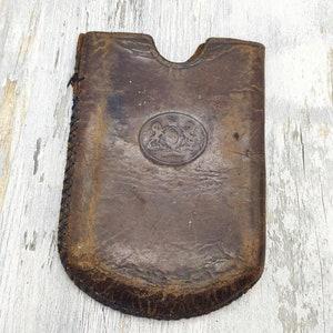 Puede incluir: Una funda de cuero marrón con un borde cosido y un diseño circular en relieve en el centro.