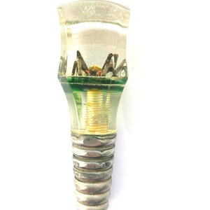 May include: A clear glass bottle stopper with a decorative spider design encased within. The stopper has a green base and a silver-colored screw-in base. The spider is black and red.