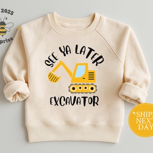 May include: Cream-colored sweatshirt with a yellow excavator graphic and the text "See Ya Later Excavator." The design includes a cartoon bee and the words "surprise" and "est 2025."