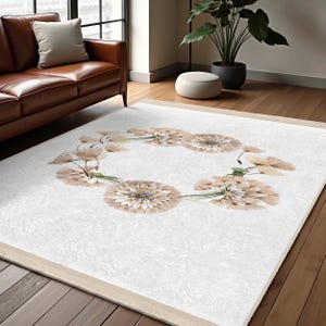 Könnte beinhalten: Ein rechteckiger weißer Teppich mit beigem Rand und floralem Design. Der Teppich zeigt eine kreisförmige Anordnung von beigen und hellbraunen Blumen mit grünen Stielen. Der Teppich liegt auf einem Parkettboden in einem Wohnzimmer.