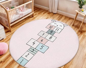 May include: A pink and white round play mat with a hopscotch design featuring a bunny rabbit and numbers 1 through 11.