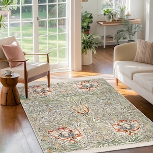 May include: A cream-colored rug with a floral pattern featuring green leaves and orange flowers. The rug is laid out on a hardwood floor in a living room setting.