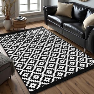 Könnte beinhalten: Schwarz-weißer geometrischer Teppich mit schwarzem Rand. Der Teppich liegt auf einem Holzboden in einem Wohnzimmer mit einem schwarzen Ledersofa im Hintergrund.