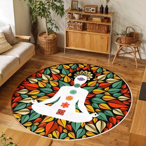 May include: Circular yoga mat with a white meditating figure and chakra symbols. The mat is decorated with a vibrant leaf design in red, orange, yellow, and green. The mat is designed for yoga and meditation.