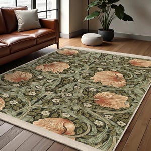 Könnte beinhalten: Ein Teppich mit floralem Muster und cremefarbenem Rand. Der Teppich zeigt ein sich wiederholendes Muster aus grünen Blättern, Ranken und orangefarbenen Blumen. Der Teppich liegt auf einem Holzboden.