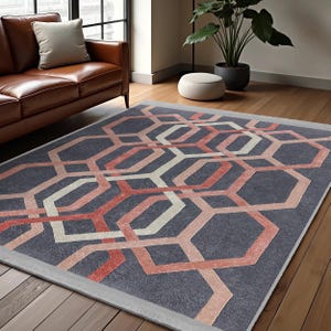 May include: A geometric patterned rug with a gray background, pink and white lines, and a subtle sheen. The rug is laid out on a wooden floor in a living room setting.