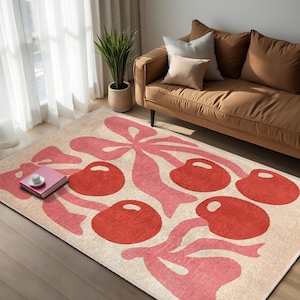 Può includere: Un tappeto color crema con un motivo di ciliegie rosa e rosse. Il tappeto presenta ciliegie stilizzate con steli e foglie, creando un motivo fantasioso e moderno.