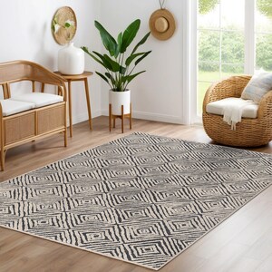 May include: A black and white geometric patterned rug with a cream background. The rug is in a living room setting with a wicker chair and a potted plant.