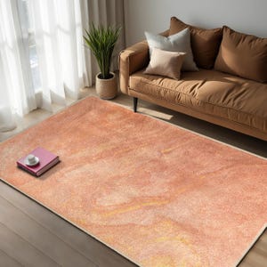 May include: A light pink and orange area rug with a marbled pattern. The rug is laid out on a wooden floor in a living room setting.