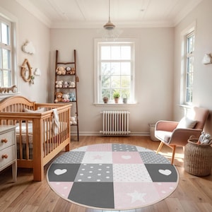 May include: A round, multi-colored patchwork rug with pink, gray, and white squares featuring stars and hearts. The rug is in a nursery with a crib and a rocking chair.