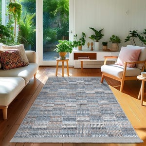 May include: A blue and beige patterned area rug with a light grey border. The rug is laid out on a hardwood floor in a living room setting.