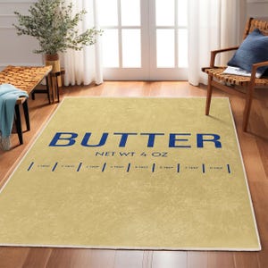 以下が含まれることがあります： ベージュのエリアラグに、青い「BUTTER」の文字と「NET WT 4 OZ」の文字が書かれています。ラグは白い縁取りと、大さじの目盛りが付いた青い線が付いています。
