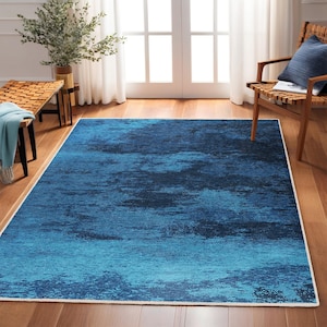 May include: A blue and teal abstract area rug with a white border. The rug has a distressed, faded look, giving it a vintage feel.