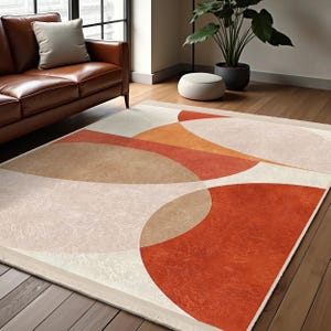 Op de afbeelding: Abstract vloerkleed met een geometrisch ontwerp met overlappende cirkels in tinten oranje, bruin en wit op een crème achtergrond.