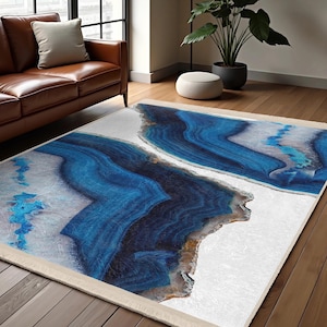Può includere: Tappeto da area astratto con sfondo bianco e design in agata blu. Il tappeto ha un bordo a frangia.