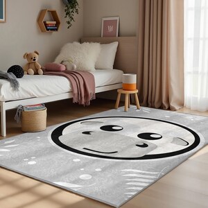 May include: A gray and white area rug with a black and white cartoon cow face design. The rug has a white background with gray and white leaf patterns.