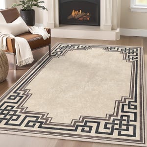 May include: A beige area rug with a black and gray geometric border. The border features a repeating pattern of interlocking squares and rectangles.