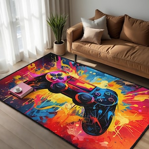 Peut inclure: Tapis rectangulaire avec un motif abstrait coloré d'une manette de jeu vidéo. Le tapis a une bordure noire et un mélange vibrant d'éclaboussures de peinture rouge, orange, jaune, bleu et rose.