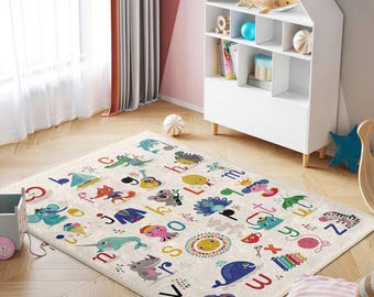 May include: A colorful alphabet playmat with a white background and illustrations of animals, letters, and objects. The playmat is on a light beige carpet in a room with a white bookshelf and a white wall.