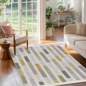 May include: A white, gray, green, and yellow patterned area rug with a geometric design. The rug is in a living room setting with a couch and a chair.