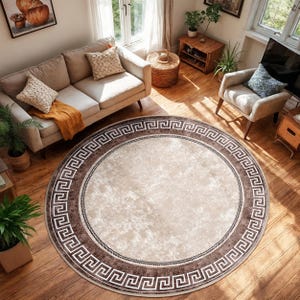 Könnte beinhalten: Ein runder Teppich mit beigefarbenem Zentrum und einem dunkelbraunen Rand mit einem griechischen Schlüsselmuster. Der Teppich liegt auf einem Holzboden, und der Raum umfasst ein Sofa, einen Sessel und natürliches Licht.
