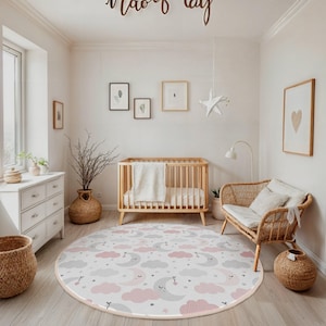 May include: A nursery room with a round rug featuring a pattern of pink and gray clouds, crescent moons, and stars. The room includes a wooden crib, a wicker chair, and a white dresser. The words "Maoof day" are written on the wall.