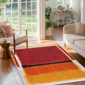 Pode incluir: Tapete de área abstrato com fundo branco e design vermelho, laranja e amarelo. O tapete tem uma faixa preta no meio.