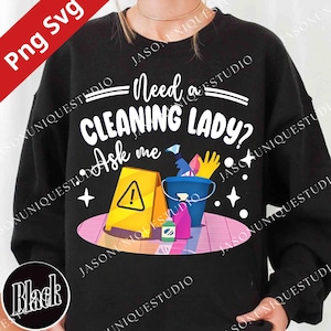 May include: Black sweatshirt with the text "Need a CLEANING LADY? Ask me." The design includes a yellow caution sign, a blue bucket with cleaning supplies, and stars. The words are in white.