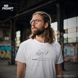 Op de afbeelding: Wit T-shirt met een zwart-witte lijntekening van een retro gameconsole en controller. Het shirt heeft ook de tekst "/prompt" en "WHERE TECH MEETS STYLE >_".