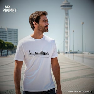Op de afbeelding: Wit T-shirt met een zwarte skyline-afbeelding en de tekst "/prompt". Het shirt heeft ook de tekst "MR PROMPT" linksboven. Het shirt wordt buiten gedragen op een zonnige dag.