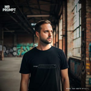 May include: A black t-shirt featuring the text "/prompt" and a search bar graphic. The person is wearing the shirt in an industrial setting. The words "WHERE TECH MEETS STYLE >_" are at the bottom.