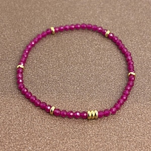 Könnte beinhalten: Ein Armband aus rosafarbenen Edelsteinen mit goldenen Akzenten. Das Armband besteht aus kleinen, facettierten Perlen und hat einen zarten, femininen Look.