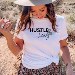 May include: White t-shirt with black text that reads "Hustle & heart" with a small heart symbol below the text.