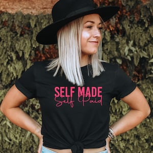 May include: A black t-shirt with the text "SELF MADE Self Paid" in pink lettering.
