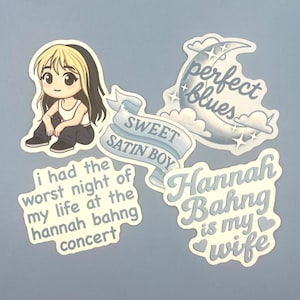 May include: A collection of stickers with various designs and text. One sticker features a cartoon character, while others display phrases like "Sweet Satin Boy" and "Perfect Blues." The stickers are in shades of blue and white.