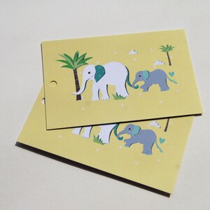 Pu&ograve; includere: Due biglietti gialli con un disegno di famiglia di elefanti. I biglietti presentano un elefante bianco con un orecchio turchese, un elefantino grigio, palme e piccoli puntini bianchi. I biglietti hanno un piccolo foro sul lato sinistro.