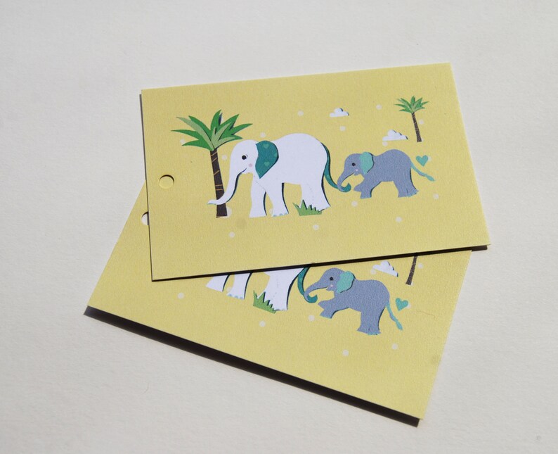 Pu&ograve; includere: Due biglietti gialli con un disegno di famiglia di elefanti. I biglietti presentano un elefante bianco con un orecchio turchese, un elefantino grigio, palme e piccoli puntini bianchi. I biglietti hanno un piccolo foro sul lato sinistro.