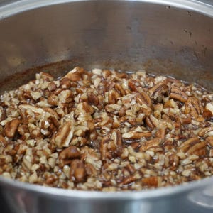 May include: A close-up of a pot filled with pecan pieces coated in a brown syrup. The pecans are evenly distributed throughout the pot.
