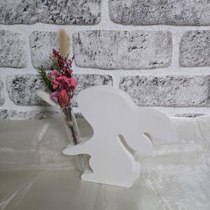 Può includere: Vaso di ceramica bianca a forma di coniglio con un tubo di vetro per i fiori. Il vaso contiene fiori secchi rosa e bianchi.