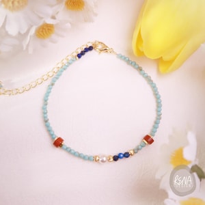 May include: Delicate beaded bracelet featuring small turquoise beads, interspersed with red and blue accent beads, and a gold clasp. The bracelet includes a small pearl and gold-colored beads. The design is elegant and suitable for everyday wear.
