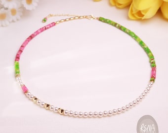 May include: A necklace featuring a mix of pink and green cylindrical beads, white round pearls, and small gold-toned heart-shaped accents. The piece includes a gold-toned metal chain extender and a clasp. The text RENA DESIGN is visible in the corner.