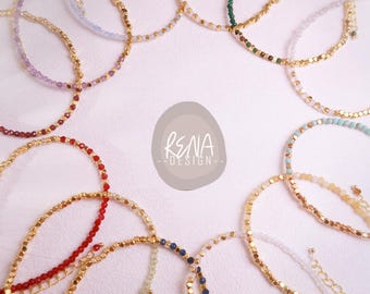 Peut inclure: Une collection de bracelets délicats disposés en cercle, composés de petites perles facettées colorées et de perles intercalaires dorées métalliques. Chaque bracelet comprend une fine chaînette d'extension dorée. Le texte RENA DESIGN est au centre.