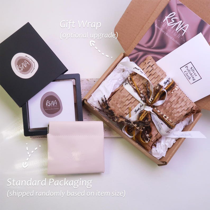 Peut inclure: Vue a&eacute;rienne des options d'emballage de produits. Une bo&icirc;te noire avec un logo est ouverte &agrave; c&ocirc;t&eacute; d'une petite pochette beige. Un coffret cadeau avec un ruban et un chiffon de polissage argent&eacute; est &eacute;galement visible. L'emballage comprend le logo de la marque.